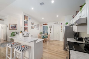 Una cocina moderna con una isla central, taburetes de bar, un comedor con mesa y sillas, y un refrigerador.