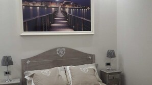 A bedroom with a bed, two bedside tables, a nightstand, a framed picture of a bridge at night, and a night lamp on each table. - Veronica's B&B (Lesina)