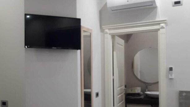 A modern bathroom with a flat-screen TV mounted on the wall, a mirror, a toilet, and a sink. - Veronica's B&B (Lesina)