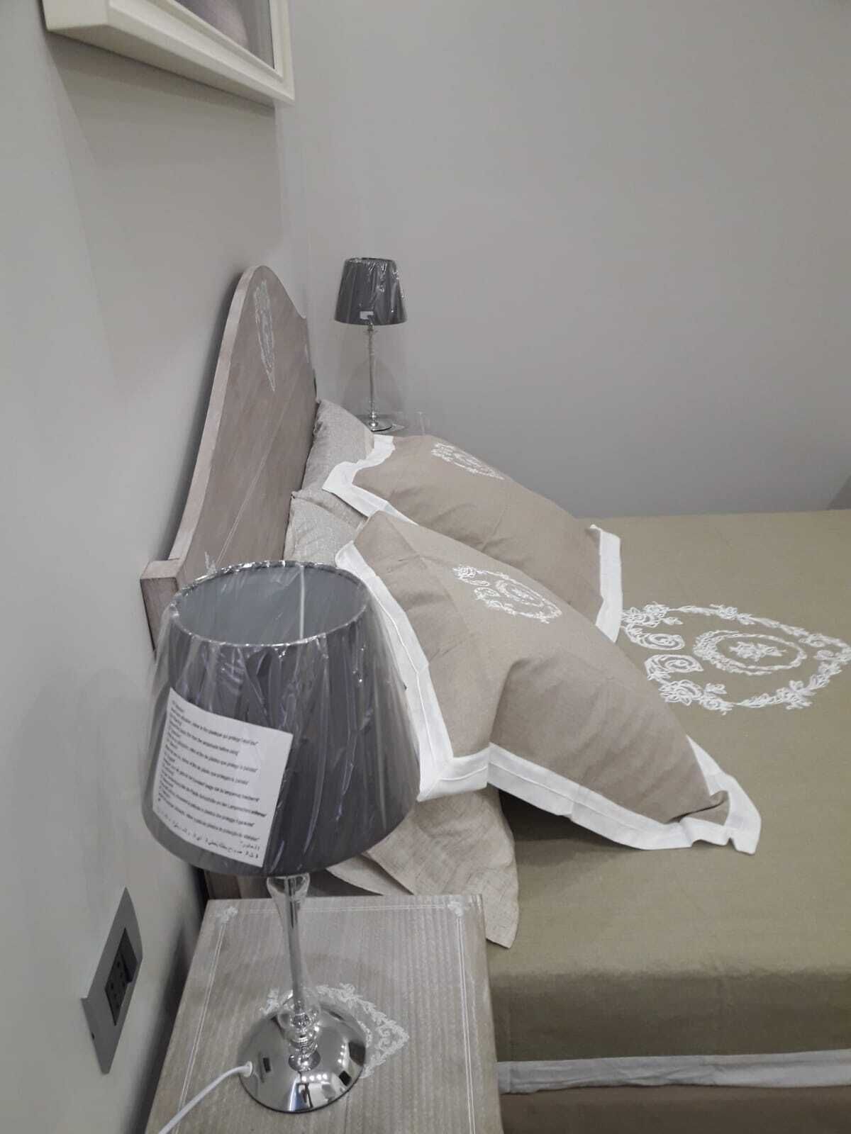 A neatly made bed with a patterned bedspread and pillows, a bedside lamp, and a small table with a lamp on it.
