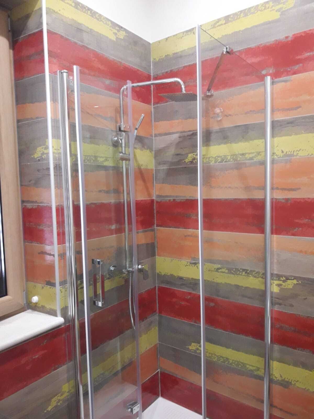 Una ducha con cerramiento de vidrio y un llamativo diseño de pared a rayas.