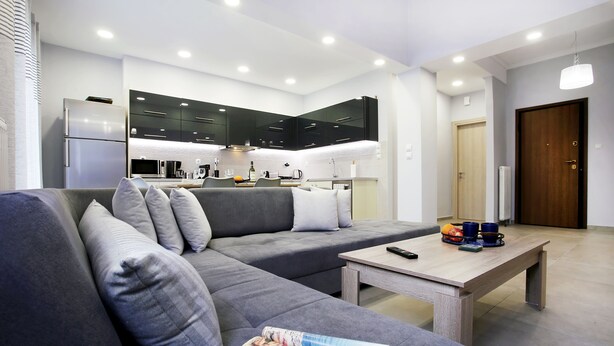 A modern living room with a grey sectional sofa, a wooden coffee table, and a kitchen in the background. - Spacious 3-Bedroom Apartment Near the Train (Athens)
