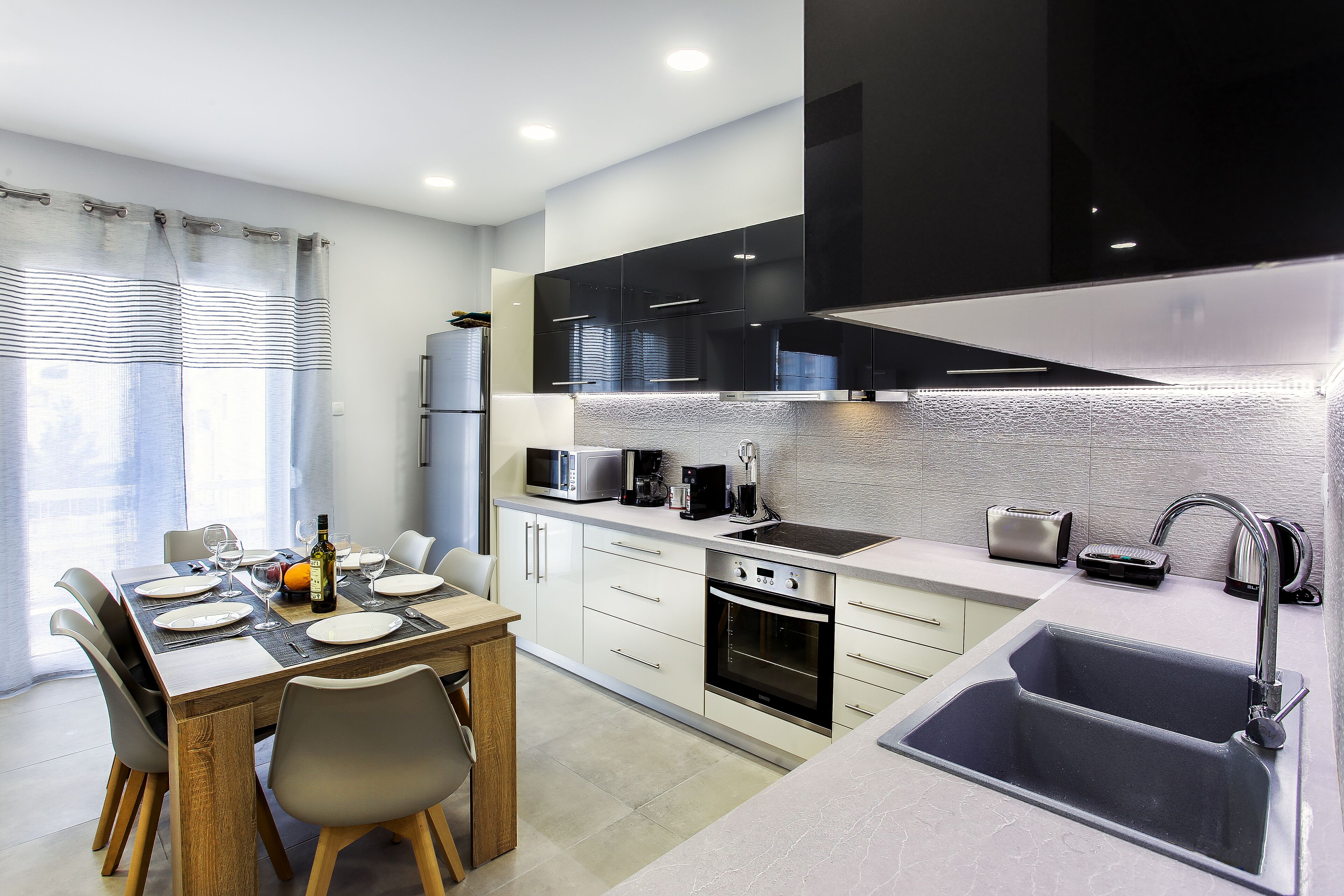 A modern kitchen with a dining area, featuring a built-in oven, a sink, and a microwave.