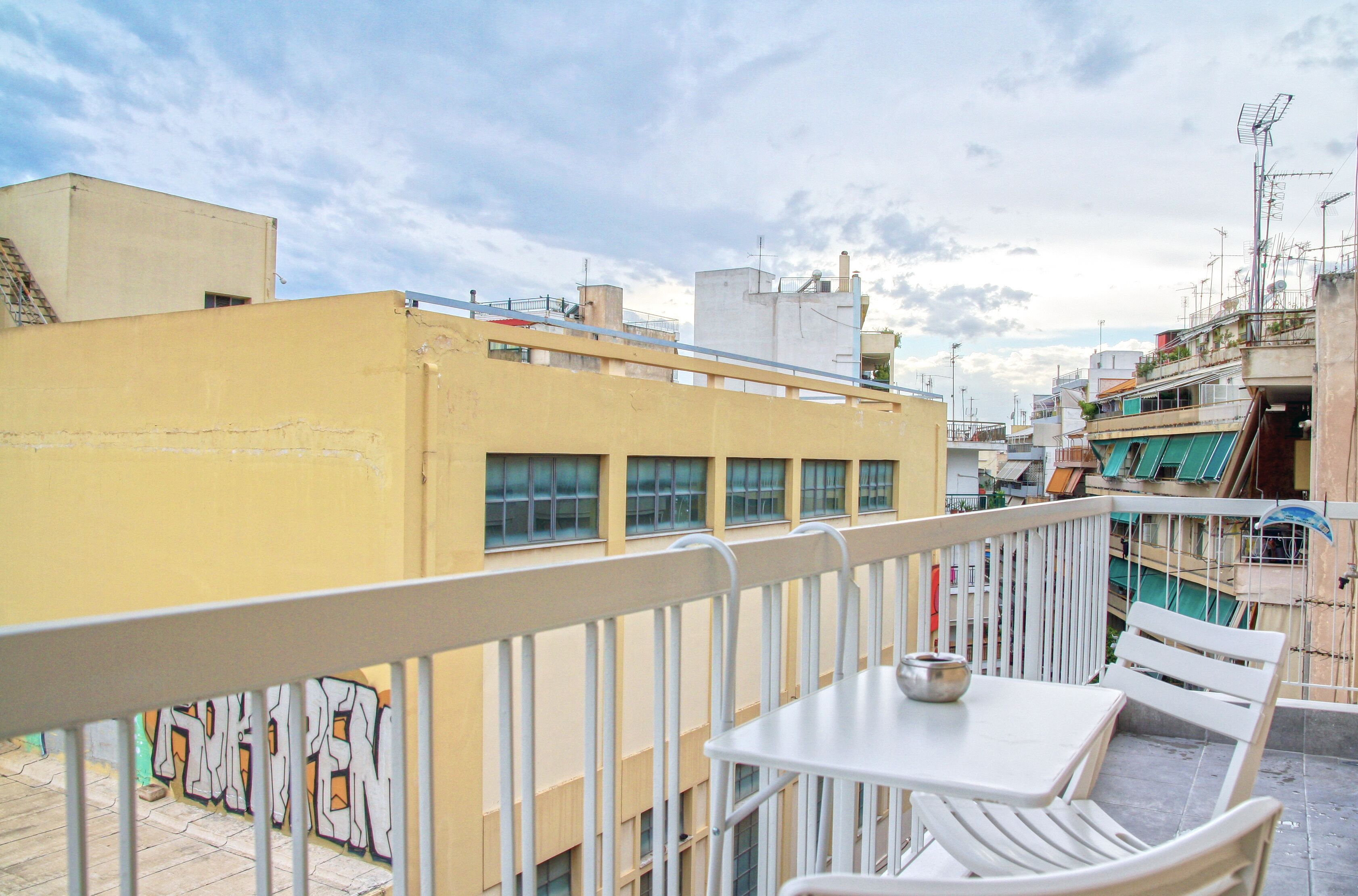 A rooftop terrace with a table and chairs, a railing, and a view of adjacent buildings.