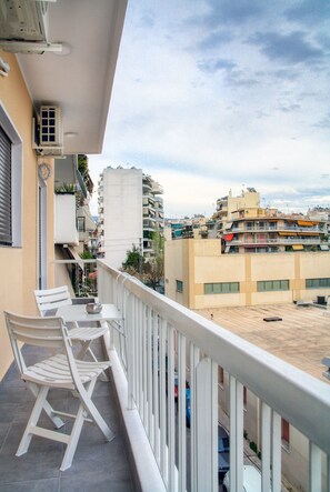 A balcony with white chairs and a table, overlooking a cityscape with multi-story buildings. - Spacious 3-Bedroom Apartment Near the Train (Athens)