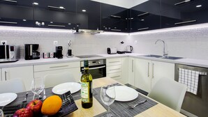 A modern kitchen with black cabinets, a stainless steel sink, and a dining area with a table set for two. - Spacious 3-Bedroom Apartment Near the Train (Athens)