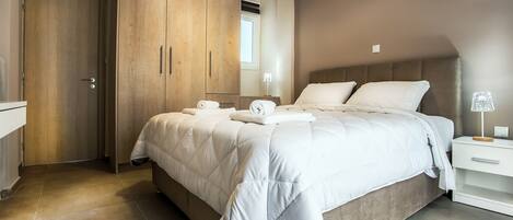 A bedroom with a large bed, a wooden wardrobe, a bedside table with a lamp, and a bathroom door.