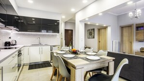 A modern kitchen with white cabinets, a wooden dining table set for four, and a built-in oven. - Spacious 3-Bedroom Apartment Near the Train (Athens)