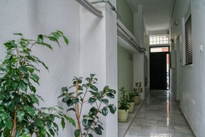 A corridor with potted plants, a tiled floor, and a door at the end. - Spacious 3-Bedroom Apartment Near the Train (Athens)