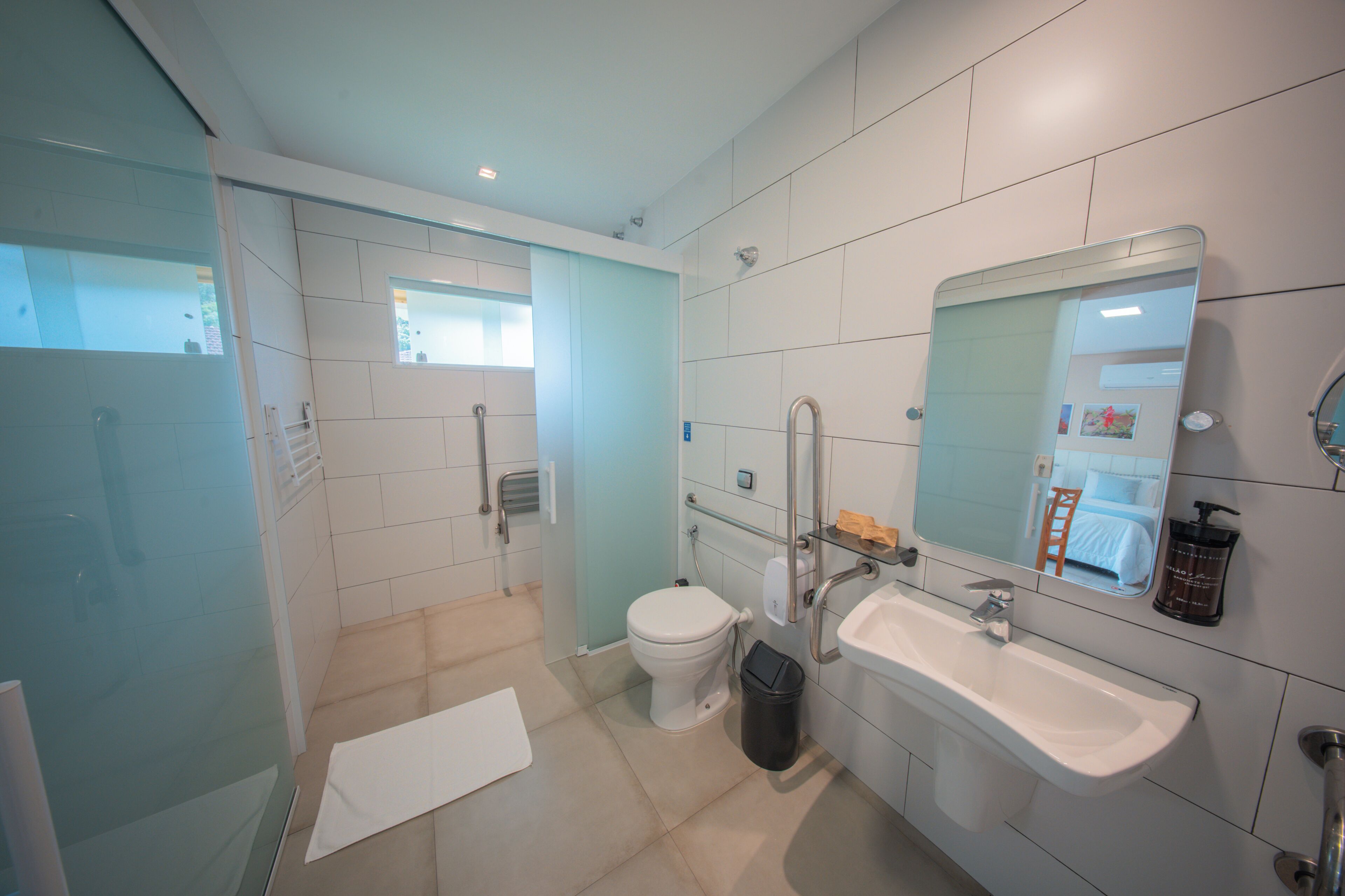 Een moderne badkamer met een douchecabine van glas, een wit toilet, een wastafel met spiegel en een prullenbak.