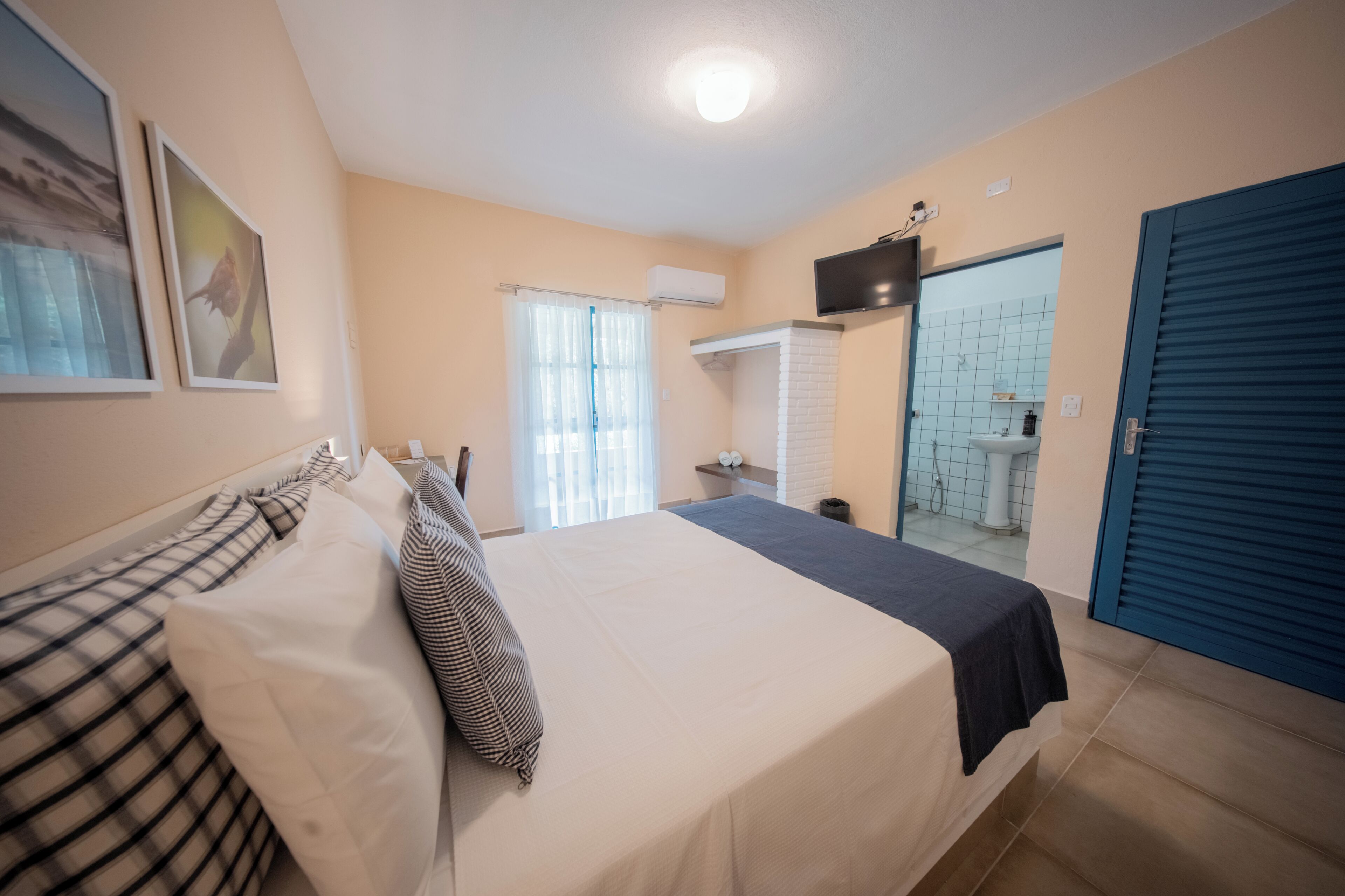 A bedroom with a bed, a bathroom visible through an open door, and a TV mounted on the wall.