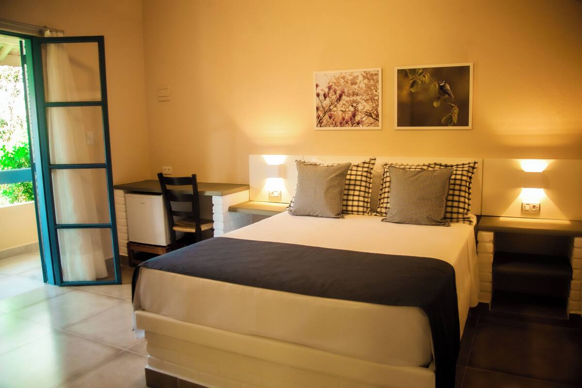 Habitación de hotel con cama, mesitas de noche, escritorio y una silla. Hay dos lámparas de pared y dos cuadros en la pared.