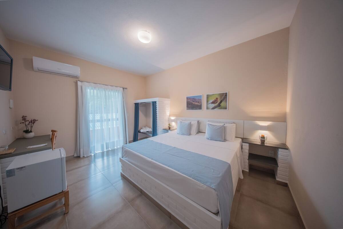 Un dormitorio con cama, mesitas de noche, escritorio, aire acondicionado, ventana con cortinas y obra de arte en la pared.