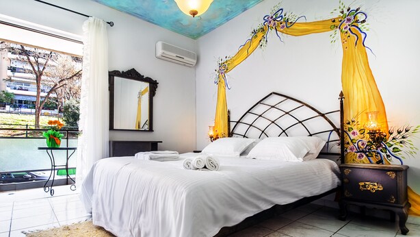 Une chambre à coucher comprenant un lit, une table de chevet, un miroir et une fenêtre donnant sur un immeuble et des arbres.