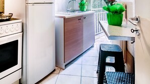 Une cuisine de taille réduite équipée d’un réfrigérateur, d’une cuisinière et d’un évier. On y trouve deux tabourets et une fenêtre avec des rideaux.
