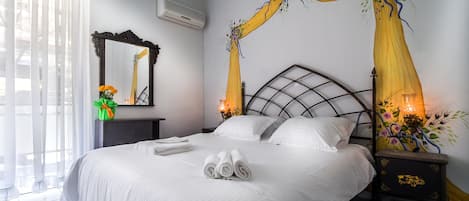 A neatly made bed with white linens, a bedside table with a lamp, and a decorative mirror on the wall.