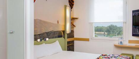 Habitación de hotel con cama, ventana con vistas, televisor y un cuadro de paisaje montañoso en la pared.