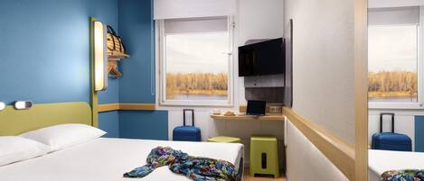 A compact hotel room with two beds, a small kitchenette, a TV, and a window with a view of trees.