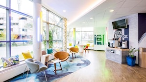 Un espacio de oficina moderno con ventanas amplias, una zona de recepción con televisor y un área de estar con sillas y sofá.