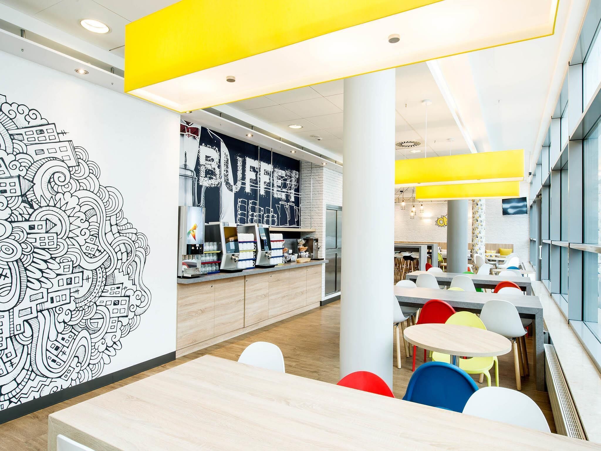 A modern cafeteria with a counter, seating area, and a large wall mural.