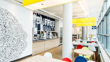 A modern cafeteria with a counter, seating area, and a large wall mural.