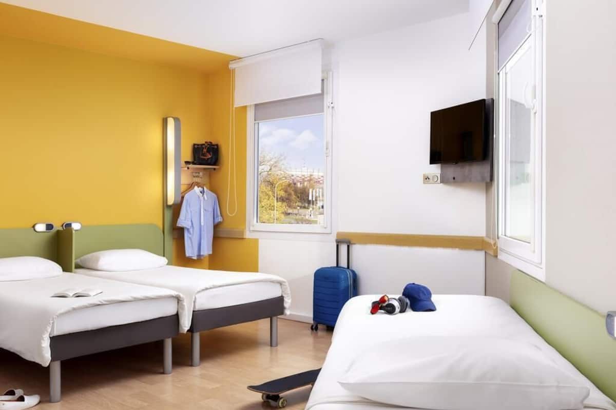 A hotel room with two beds, a window with a view, a TV, and a suitcase.