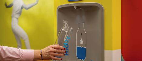 Dispensador de agua con etiqueta azul que indica ahorro de botellas de plástico.