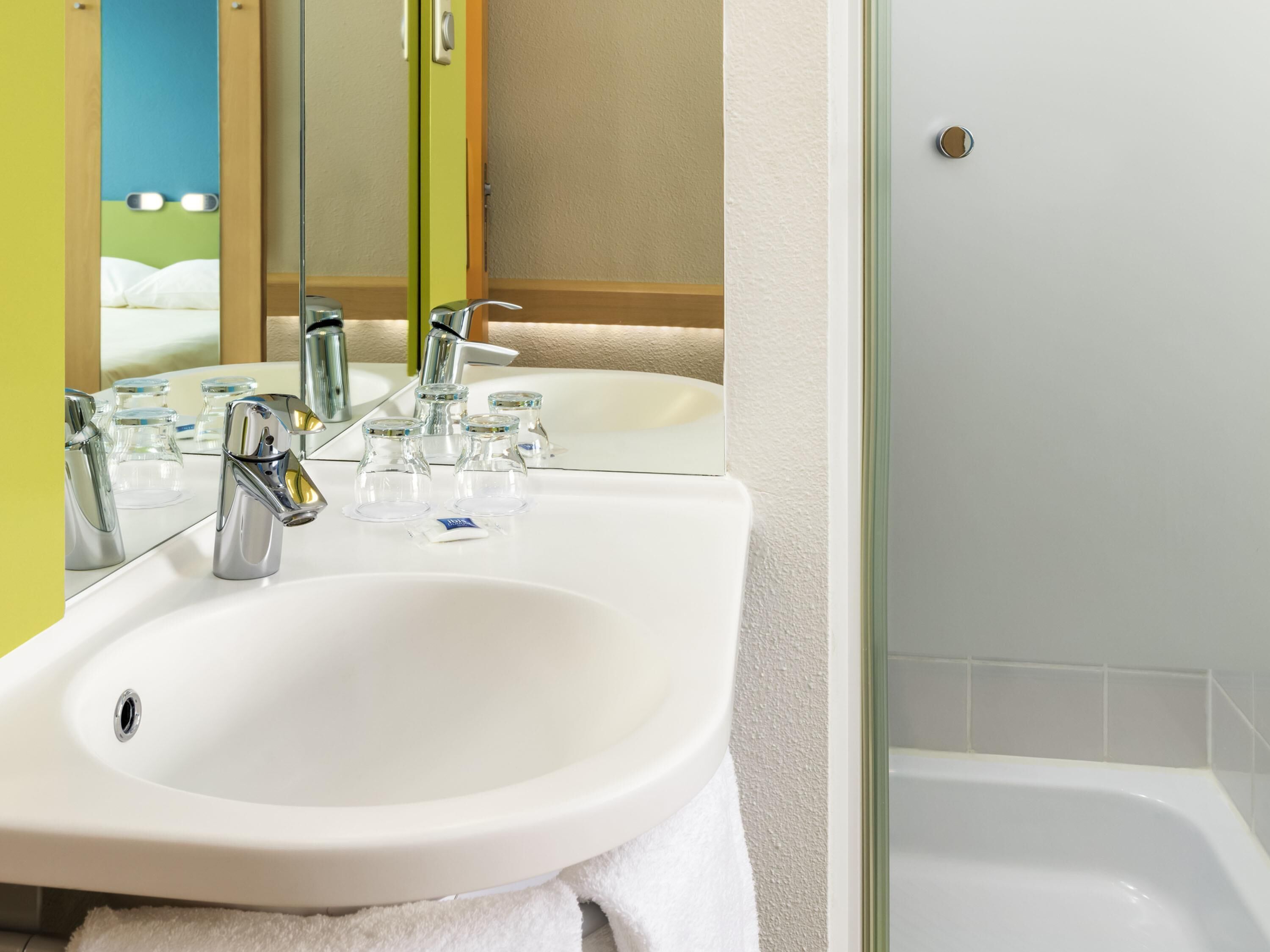 A bathroom with a white sink, a mirror, a shower, and a towel.