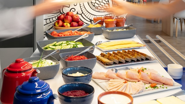 Una mesa de buffet con diversos alimentos y una mano alcanzando un bol.