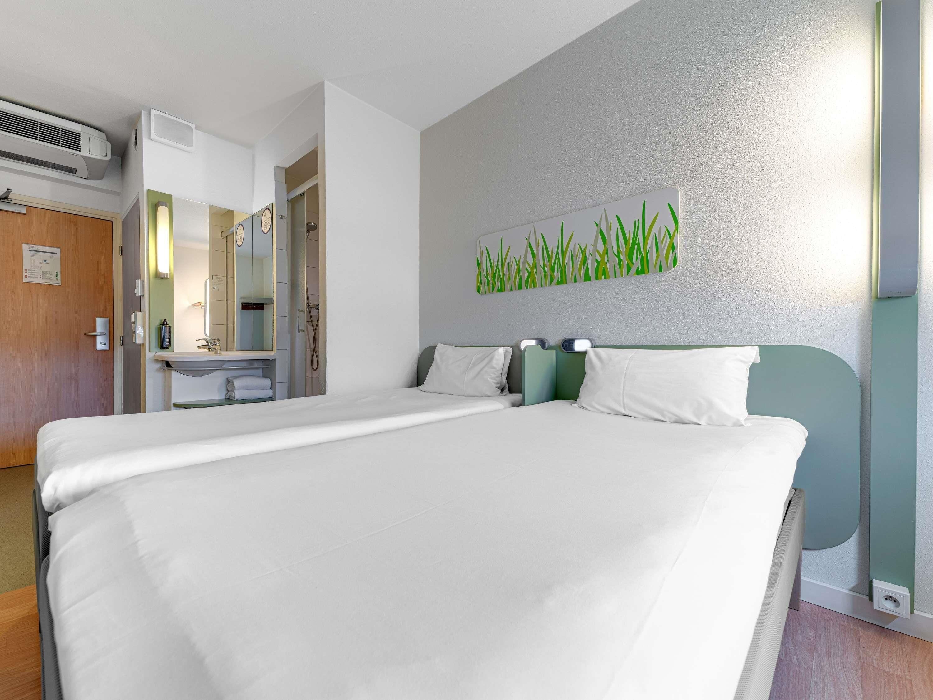 A hotel room with a bed, a bathroom with a mirror, and a wall-mounted air conditioning unit.