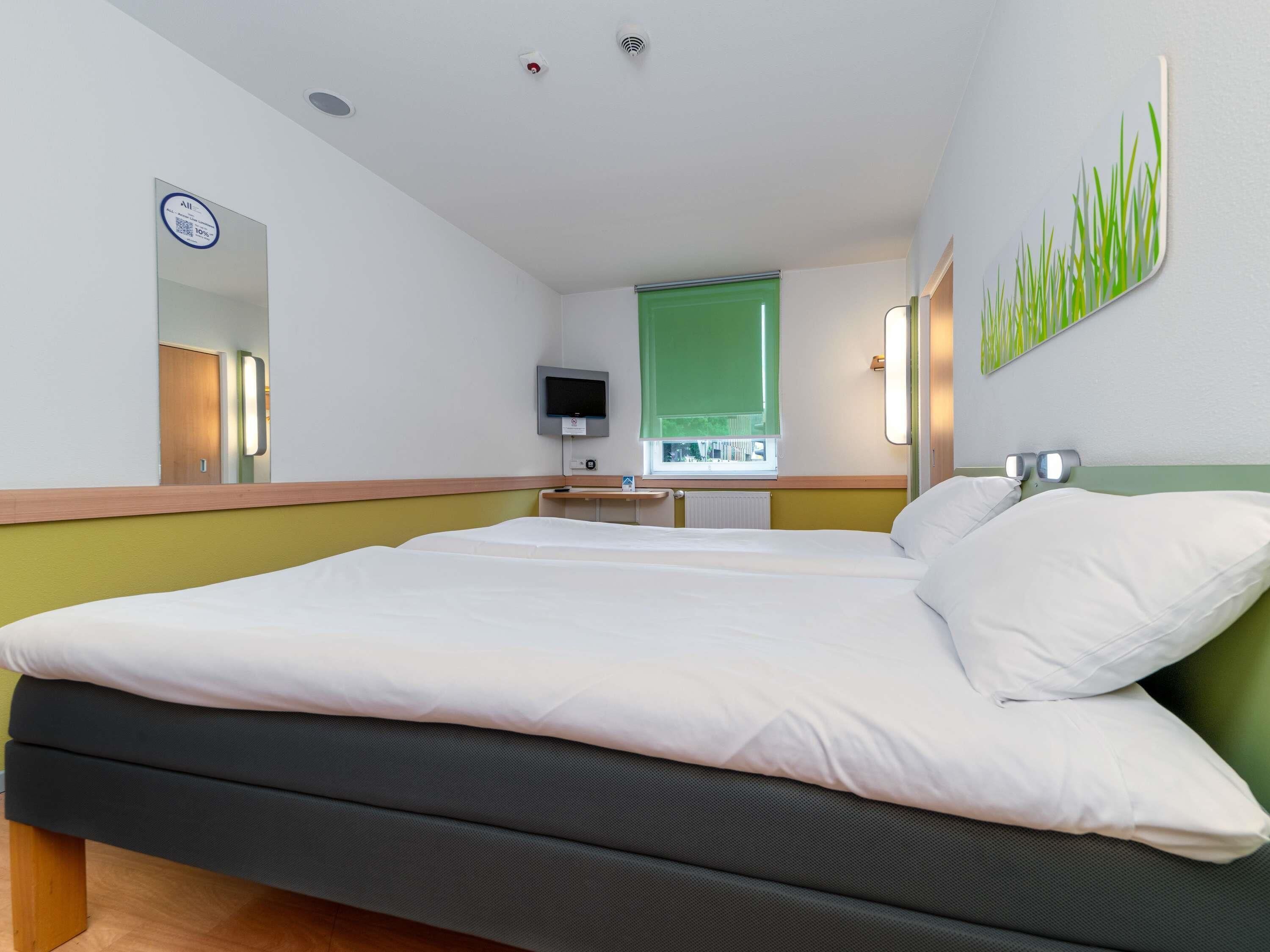 Una habitación de hotel con una cama, televisión, espejo y pared verde.