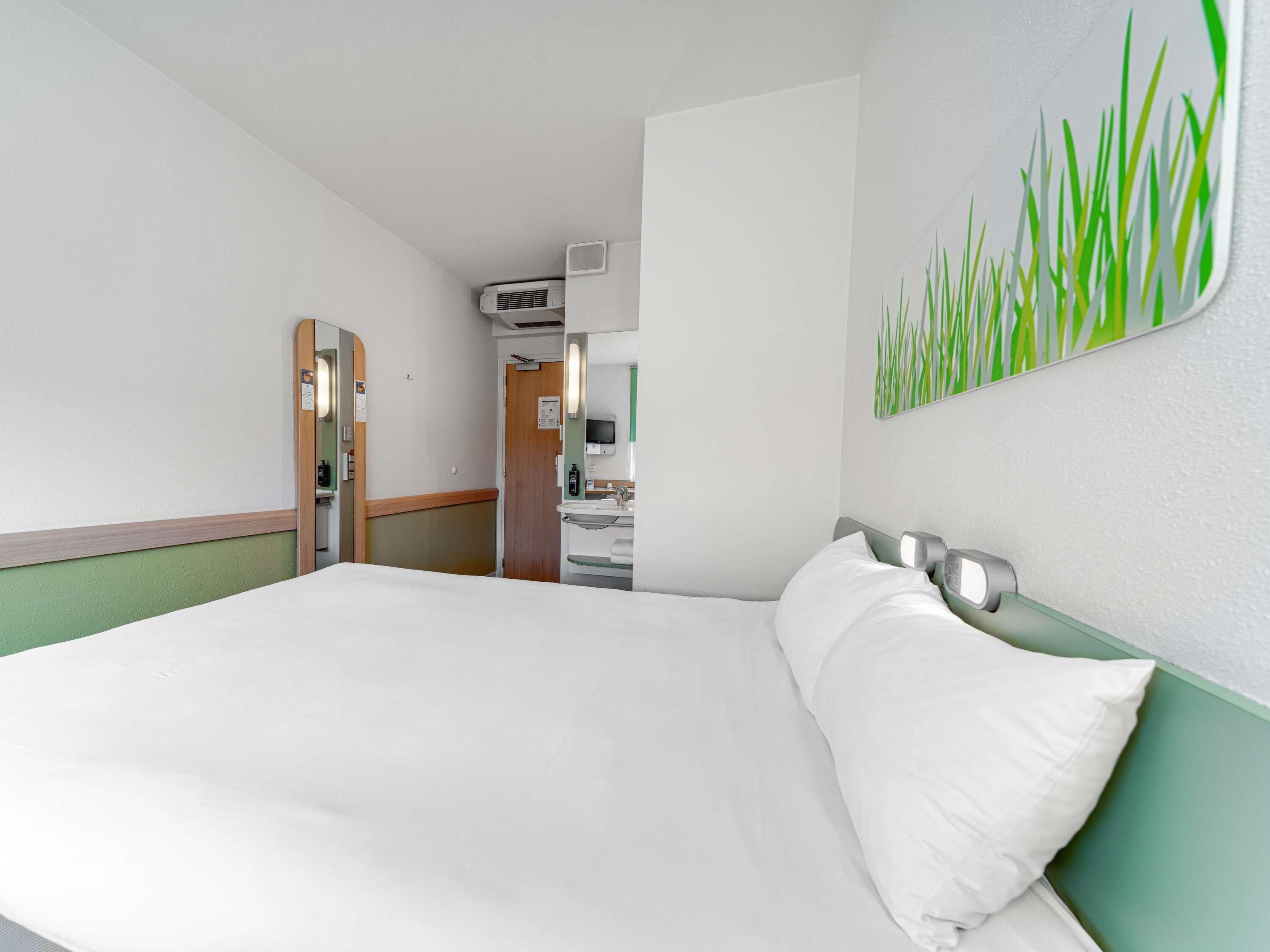 A hotel room with a bed, a bathroom with a sink and mirror, and a hallway leading to another room.