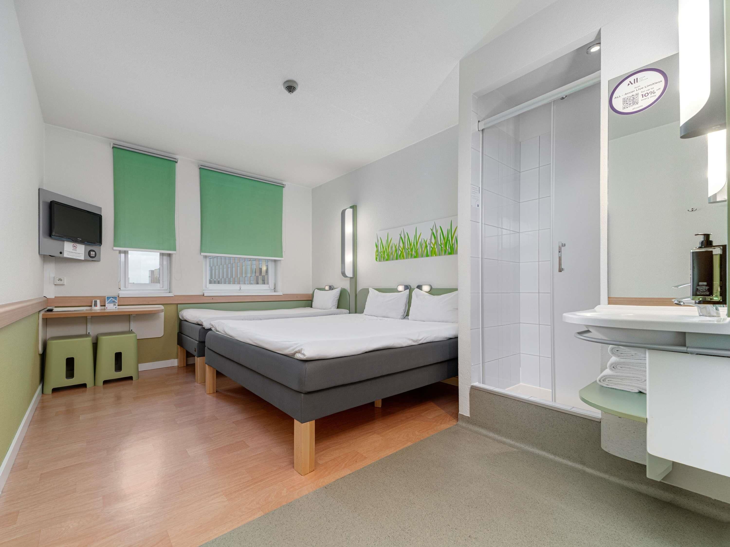 A hotel room with a bed, bedside tables, a TV, a bathroom with a sink and mirror, and a green wall decoration.
