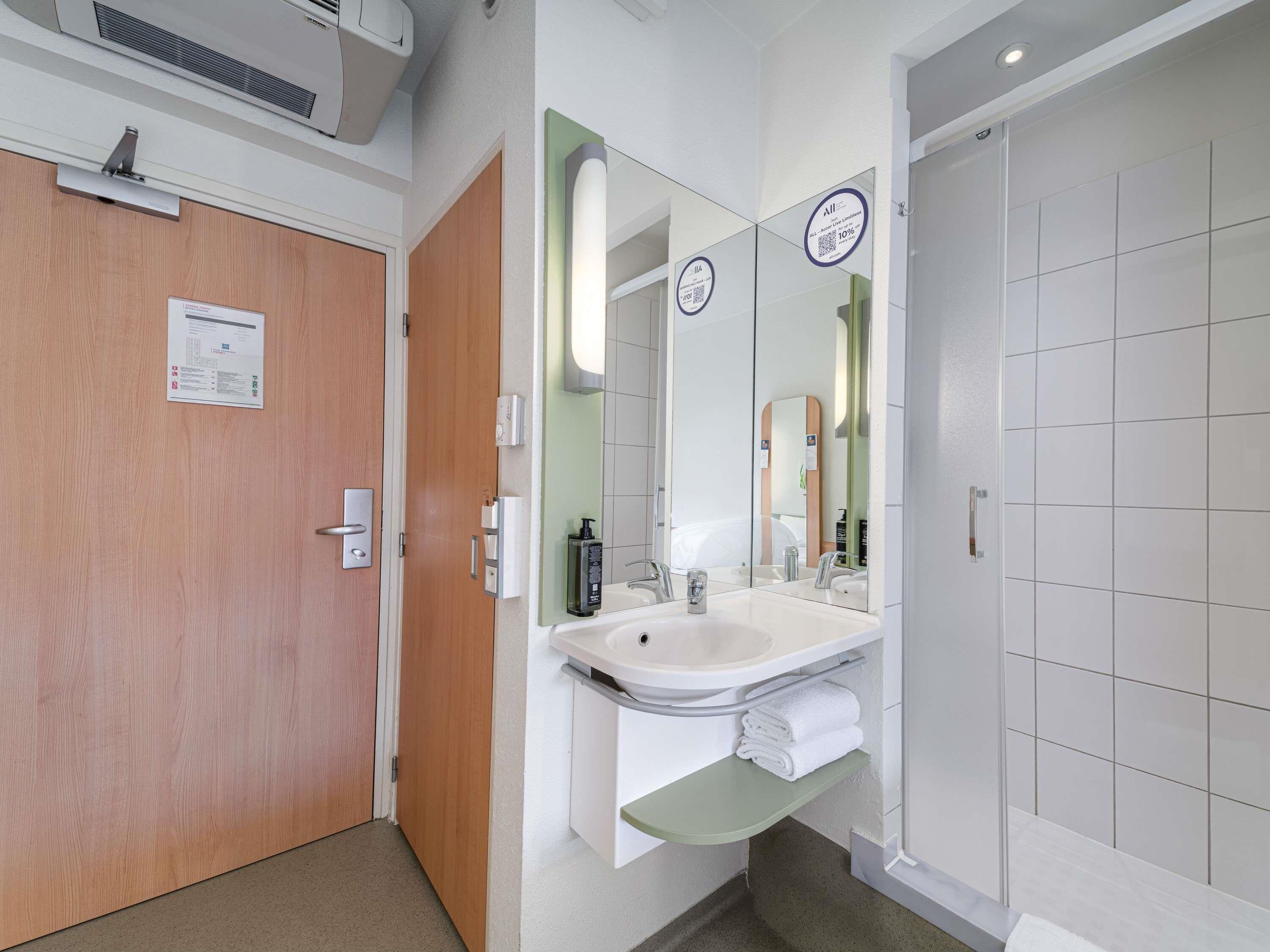 A hotel bathroom with a wooden door, a sink with a mirror, and a shower area.