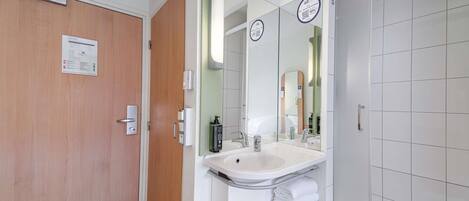 A hotel bathroom with a wooden door, a sink with a mirror, and a shower area.