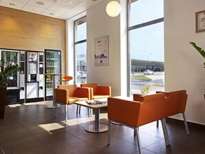 A modern hotel lobby with seating, a vending machine, and a large window with a view of the street.