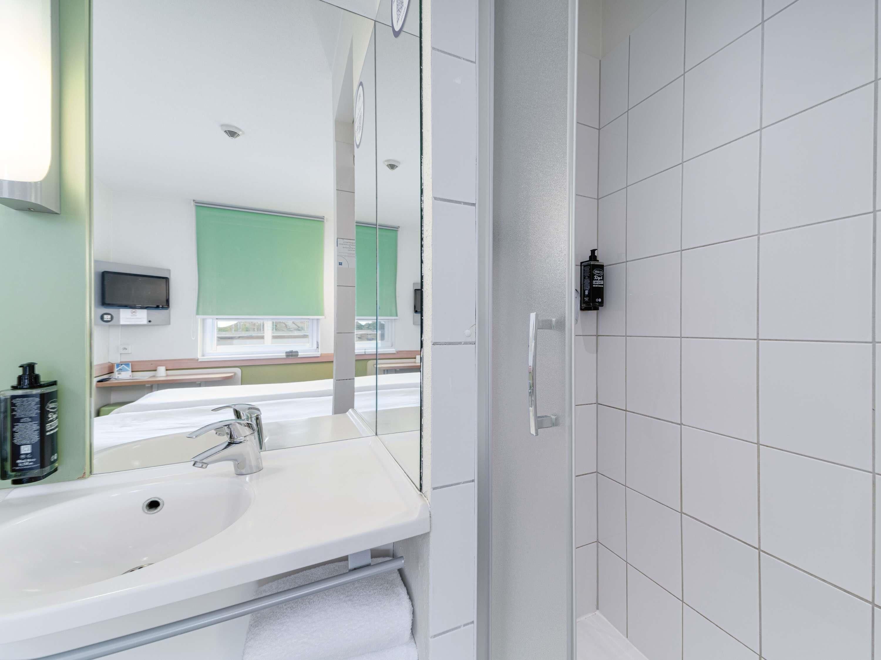 Un baño moderno con lavamanos blanco, espejo y paredes con azulejos.