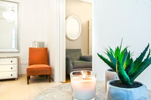 A room with a marble table, a lit candle, a potted aloe vera plant, a white dresser, and a mirror on the wall.