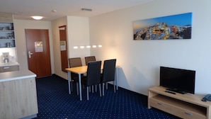 A hotel room with a dining table, chairs, a TV, and a painting on the wall. - APART HOLIDAYS Morschach (Morschach)