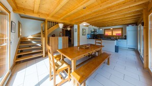 A wooden interior with a dining table, benches, a staircase, and a kitchen area.