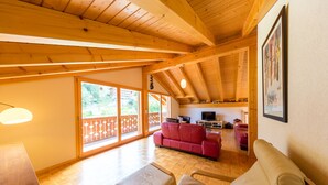 A spacious living area with wooden beams, a red sofa, a beige couch, and a television.