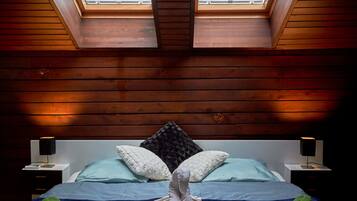 Ein Schlafzimmer mit schrägverdeckter Decke, zwei Dachfenstern, einem Bett mit Kissen, einem Nachttisch und einer Lampe.