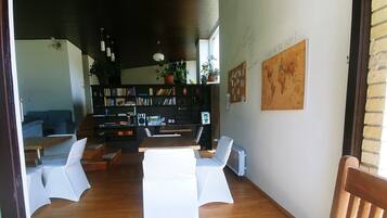 Ein modernes Wohnzimmer mit einem Holztisch, weißen Stühlen, einem Bücherregal und einer Weltkarte an der Wand.
