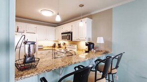 A kitchen with white cabinets, a granite countertop, a built-in microwave, a stove, and a coffee maker.