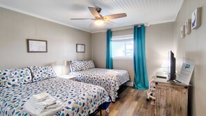 A hotel room with two beds, a ceiling fan, a TV, and a desk with a computer.