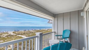 A balcony with a view of the beach, a table, and two chairs.
