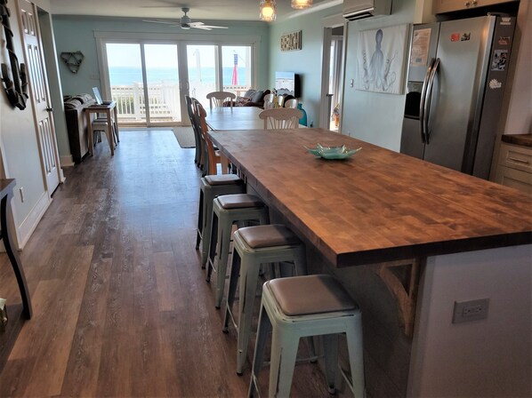 A kitchen with a wooden island, bar stools, and a view of the ocean through large sliding doors.