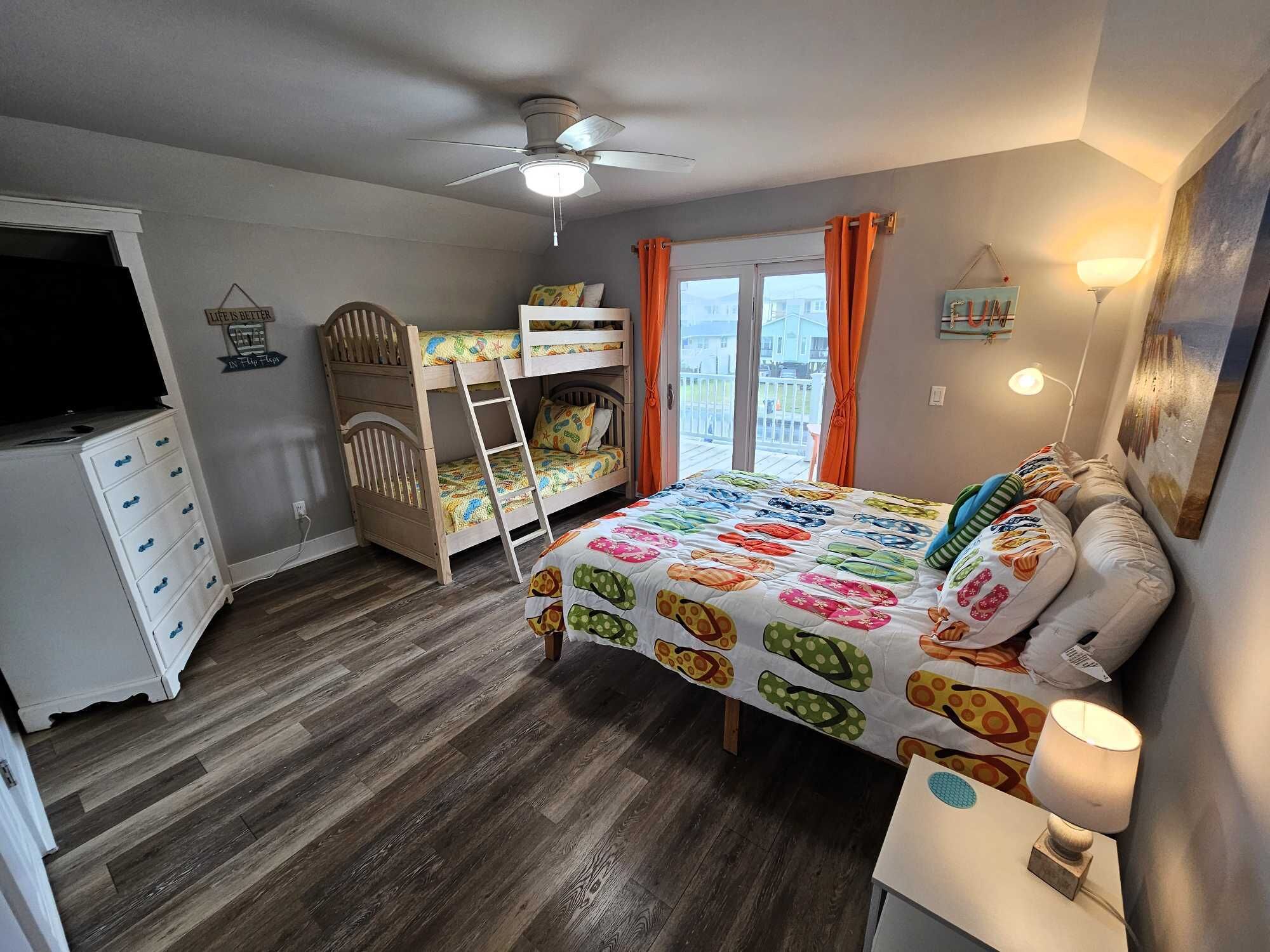 Une chambre avec un lit superposé, un bureau, une chaise, un ventilateur de plafond et une fenêtre avec des rideaux.