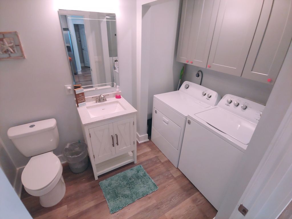 Een kleine badkamer met toilet, wastafel, spiegel en een wasmachine.