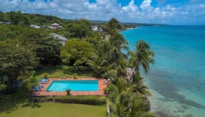 Vista aérea de un resort con piscina rodeada de palmeras y una vista despejada del océano.